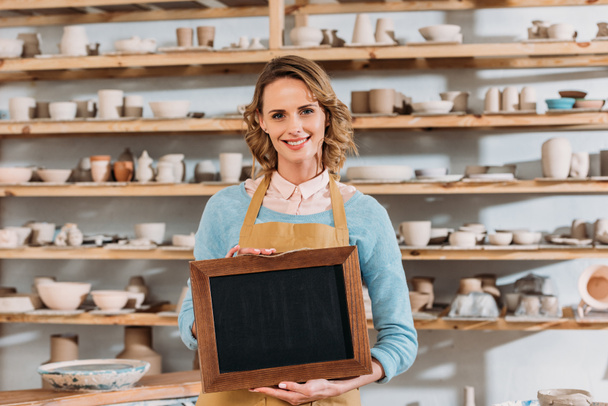 beautiful smiling owner with chalkboard in pottery workshop - Photo, Image