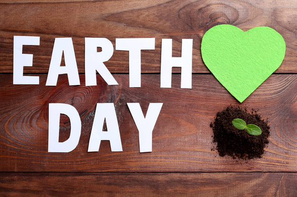 Inscription Earth Day with young plant in ground on wooden table - Фото, изображение
