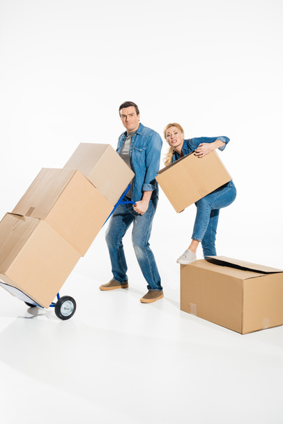 Young couple moving cardboard boxes with trolley cart isolated on white - Photo, Image