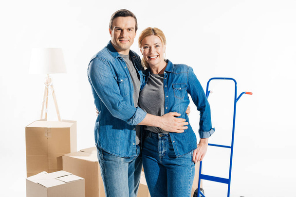 Uomo e donna sorridenti abbracciati dal carrello di consegna e scatole di cartone in movimento isolate su bianco
 - Foto, immagini