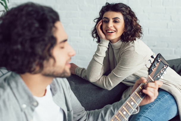 poikaystävä soittaa kitaraa ja laulaa hymyilevä tyttöystävä kotona
 - Valokuva, kuva