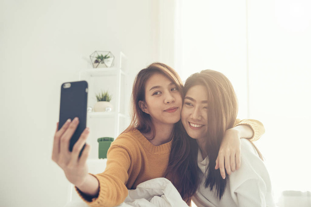 Mooie jonge Aziatische vrouwen Lgbt lesbische gelukkige paar zittend op bed knuffel en het gebruik van de telefoon nemen selfie samen slaapkamer thuis. LGBT lesbisch koppel samen binnenshuis concept. Mooie tijd thuis doorbrengen. - Foto, afbeelding