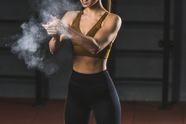 Cropped image of young sportswoman spreading chalk powder in hands for exercising in sports hall - Фото, изображение