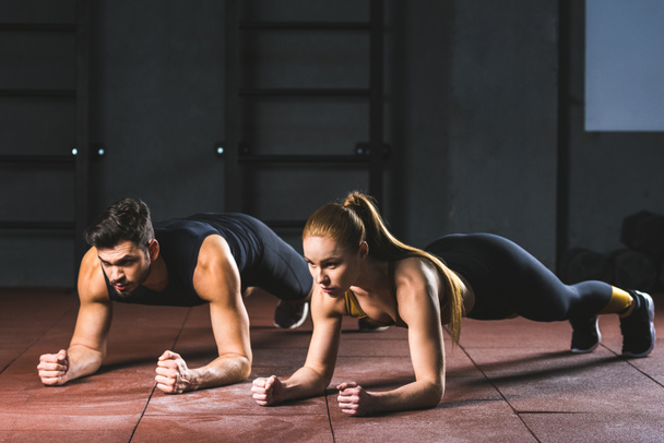 Young sportswoman and sportsman doing push ups in sports hall - Photo, Image