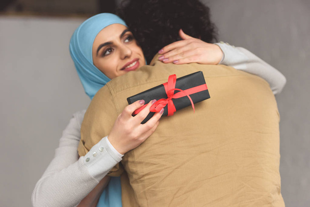 novia musulmana en hijab celebración de la caja de regalo y abrazo novio en casa
 - Foto, Imagen