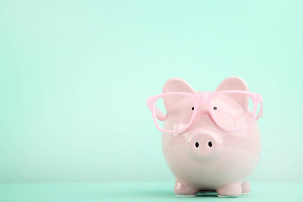 Pink piggy bank with glasses on mint background - Фото, изображение