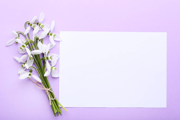 Bouquet of snowdrop flowers with blank sheet of paper on purple background - Zdjęcie, obraz