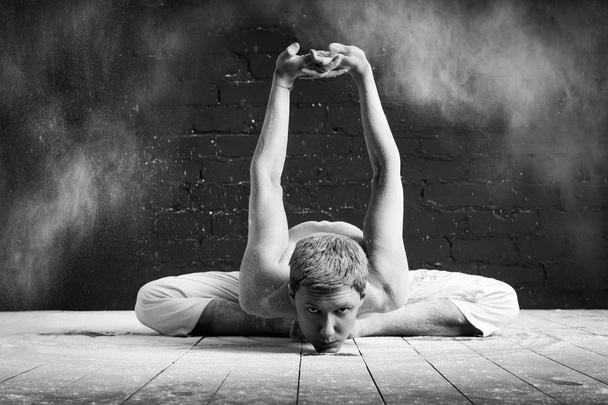 A man doing yoga in a white cloud of dust in a dark room. The concept of energy. Pada-Prasar-pashchimottanasana (pose for stretching the posterior surface of the body with legs apart) - Foto, imagen