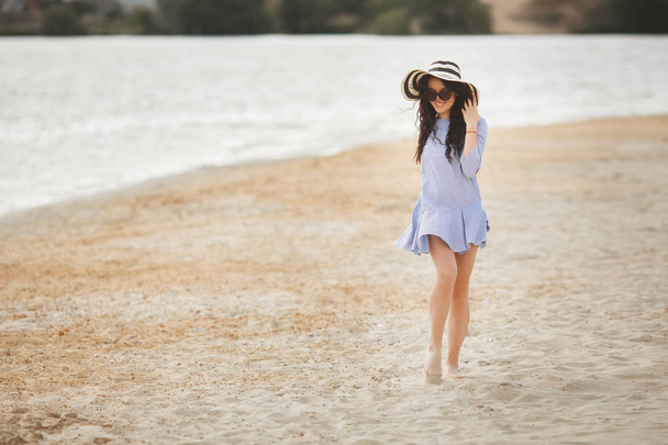 Jeune femme en grand chapeau rayé marchant sur la plage de sable
 - Photo, image