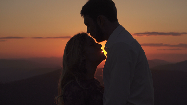 ハンサムな男は夕日の背景に額や唇に彼の恋人にキスします。. - 映像、動画