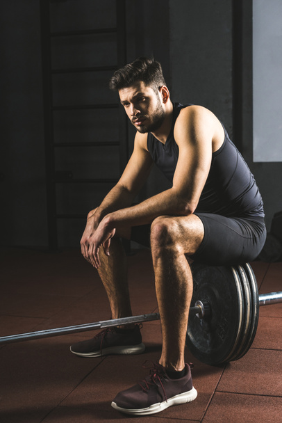 Young caucasian sportsman sitting on barbell in gym - Фото, зображення
