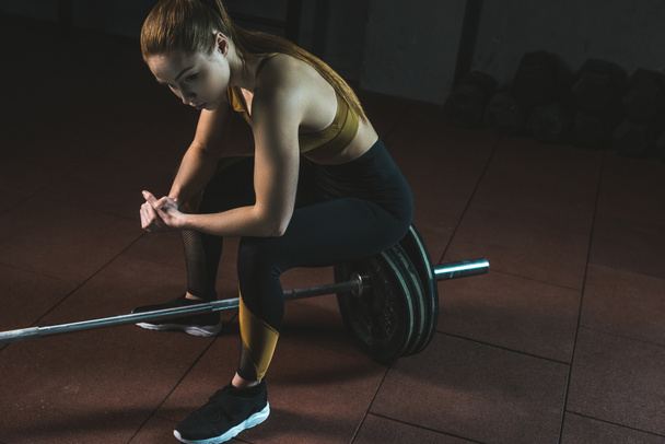 Frustrated young sportswoman sitting on barbell in gym - Фото, зображення