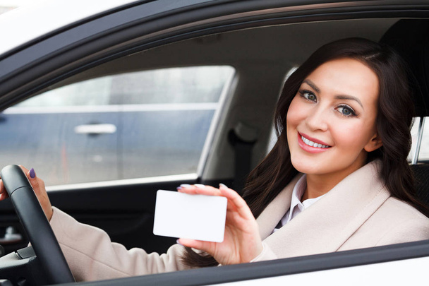 Portrait of smiling woman driver holding a white blank business card  - Foto, immagini