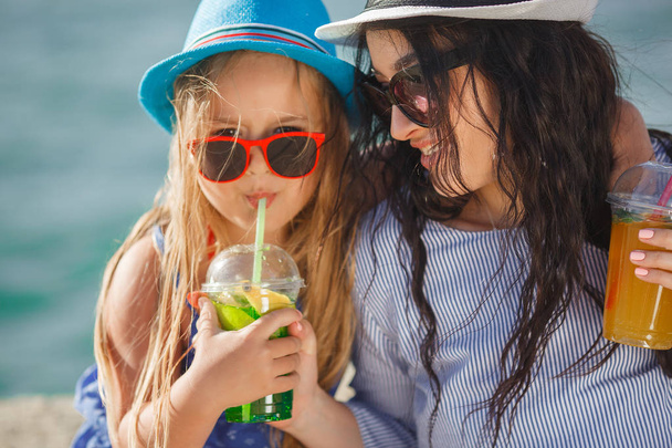 Νεαρή μητέρα με μικρή κόρη πίνοντας λεμονάδα στην παραλία - Φωτογραφία, εικόνα