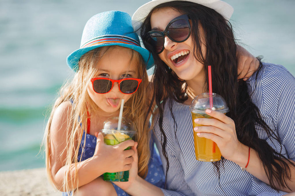Молодая мать с дочкой пьет лимонад на пляже
 - Фото, изображение