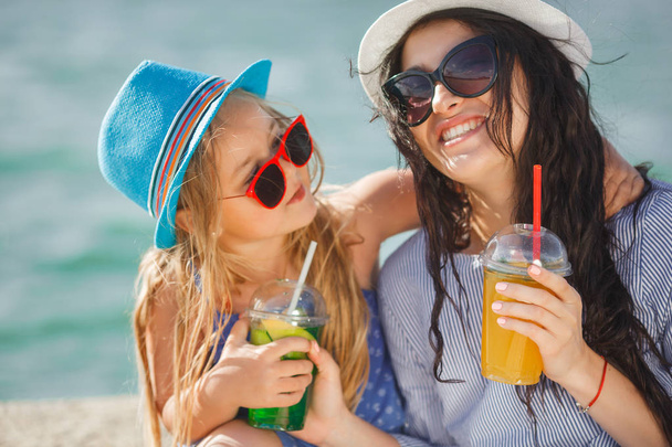 Jonge moeder met dochtertje limonade drinken op strand - Foto, afbeelding