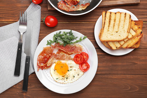 Plate with fried egg, bacon and tomatoes on wooden background - Foto, afbeelding