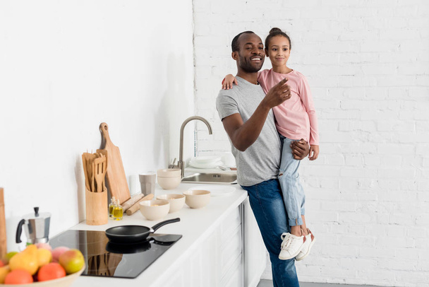 handsome father holding his daughter at kitchen and pointing somewhere - Foto, Bild