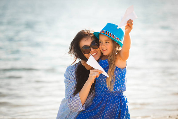 Joven madre con hija jugando con aviones de papel en la playa
 - Foto, imagen