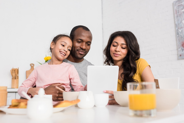 heureux jeune famille en utilisant tablette sur la cuisine tout en prenant le petit déjeuner
 - Photo, image