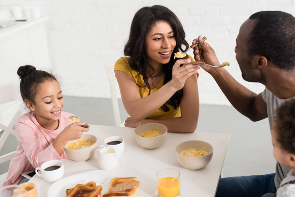 wife and husband feeding each other while having breakfast with kids - Photo, Image