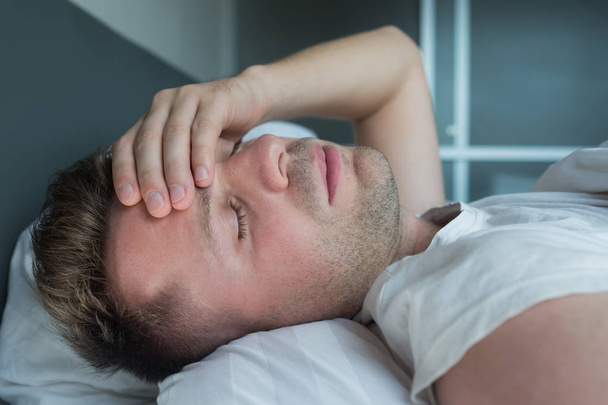 чоловік лежить в ліжку вдома страждає від головного болю або похмілля
 - Фото, зображення