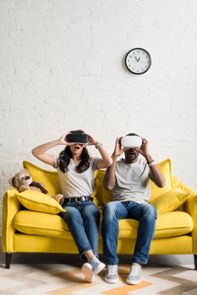 shocked african american couple in virtual reality headsets sitting on couch - 写真・画像