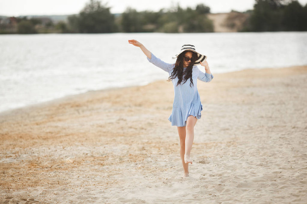 Giovane donna in grande cappello a righe a piedi sulla spiaggia di sabbia
 - Foto, immagini