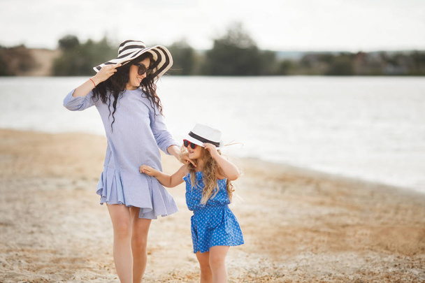 Mother in striped hat with little walking on sandy beach - Φωτογραφία, εικόνα