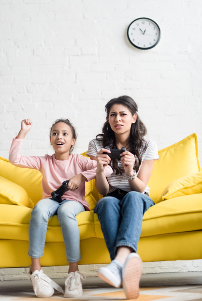 emotional mother and daughter playing video games at home on couch - Photo, Image