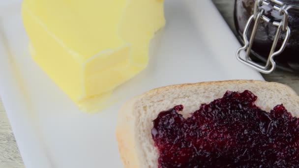 Marmelade, Butter in Butterform und Marmelade auf Toast verteilen. Gesundheits- und Ernährungskonzept. ländliche weiße Holzkulisse - Filmmaterial, Video