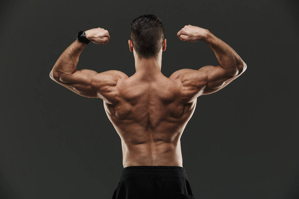 Back view of a muscular bodybuilder flexing biceps - Фото, зображення