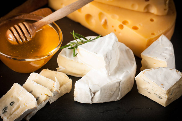 スレート板の様々 なチーズと赤いバラのワインのガラス。ブリー。カマンベール。ゴーダ、Masdaam、ロック フォール、チェダー チーズ、ナッツ、蜂蜜、クラッカー、木のブドウ ブルーチーズします。イタリア、フランスのチーズ. - 写真・画像