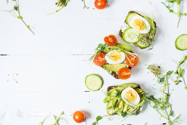 Tasty sandwiches with egg, avocado and vegetables on wooden white rustic background. - Photo, Image
