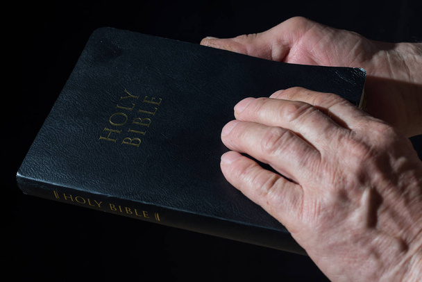 Aged mans hands holding the Bible. Low key light. - Photo, Image