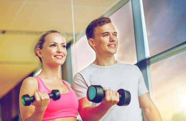 smiling young woman with personal trainer in gym - Fotografie, Obrázek