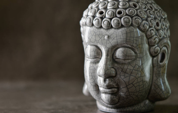 Estátua de cabeça de Buda em pé em uma superfície de pedra escura
 - Foto, Imagem