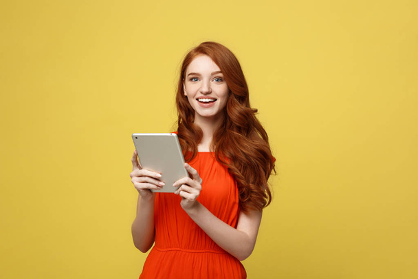 ビジネス女性、笑顔ビジネスの女性、女性のビジネス、仕事の概念: 笑顔と明るい黄色の背景に分離されたタブレットに取り組んで魅力的な赤毛の若い女性の肖像画. - 写真・画像