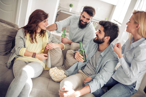 Grupo alegre de amigos bebendo cerveja e comendo pipocas em casa
 - Foto, Imagem
