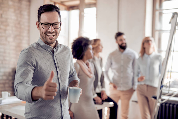 confident young businessman showing thumb up, with colleagues on background  - Photo, Image