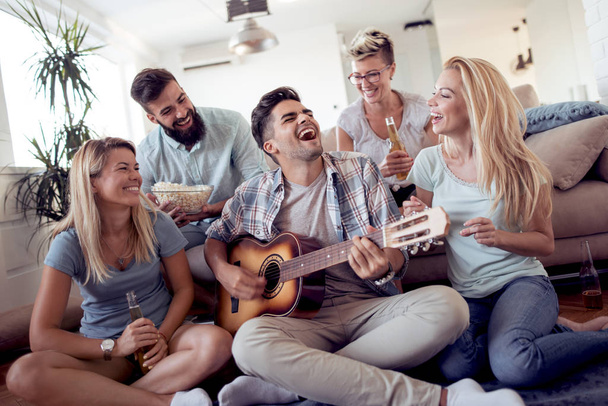 Happy jonge vrienden gitaarspelen en plezier thuis - Foto, afbeelding