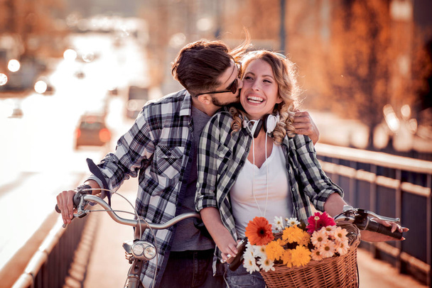 Νεαρό ζευγάρι στα ποδήλατα με λουλούδια στην πόλη - Φωτογραφία, εικόνα