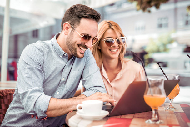 Мужчина и женщина сидят в уличном кафе и просматривают ноутбук
 - Фото, изображение