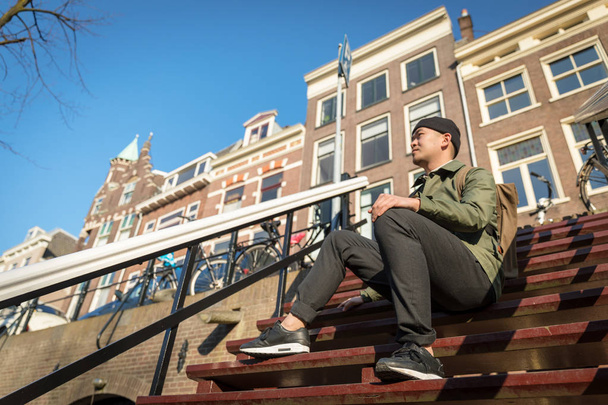 Αστική Ασίας άνδρα με σακίδιο που κάθονται στα σκαλοπάτια. Ευπαρουσίαστο. C - Φωτογραφία, εικόνα