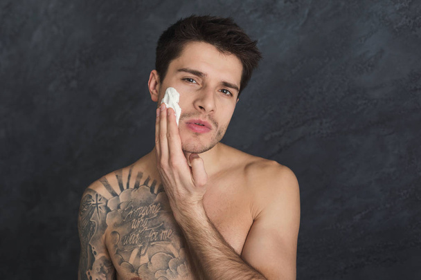 Young sexy tattooed man put foam on face - Photo, Image