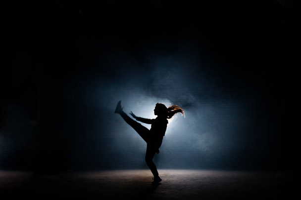 young dancer with long hair raising up her leg on dark stage - Foto, Bild