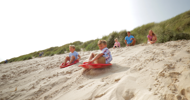 Plan au ralenti de deux frères poussés vers le bas d'une dune de sable assis sur des planches de sable, ayant une compétition
. - Séquence, vidéo