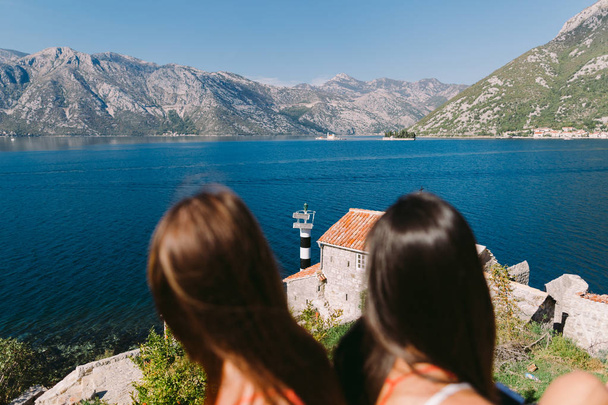 zwei Mädchen, die sich am Strand mit Blick auf die Berge entspannen. kotor bay, montenegro - Foto, Bild