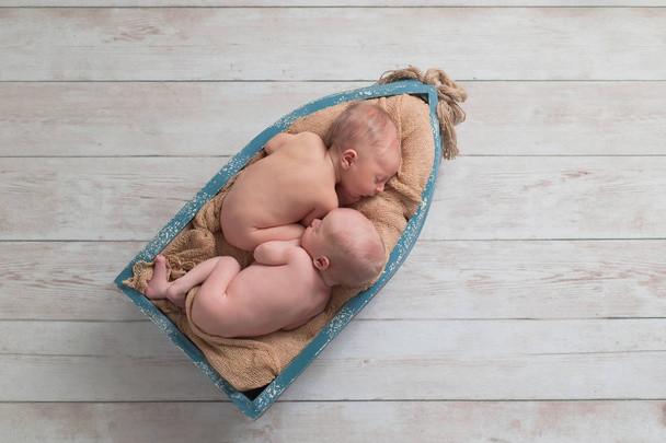 Bambini di sei giorni fraterni, gemelli, neonati, che dormono in una piccola barca di legno. Girato in studio su uno sfondo di legno
. - Foto, immagini