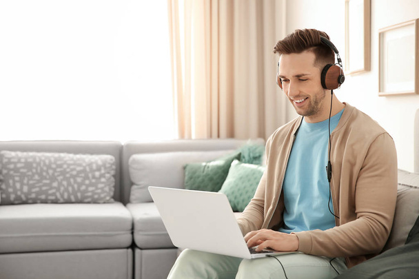 Handsome young man with laptop listening to music at home - Fotó, kép